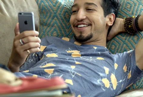 Smiling man lounging on couch looking at smart phone in one hand