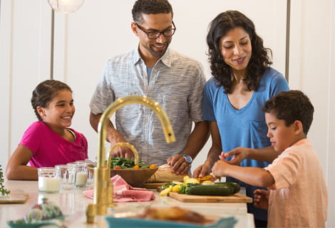 Family gathering around kitchen counter, preparing a meal.