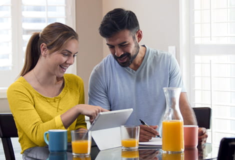 Couple sitting at breakfast table looking at smart tablet screen and smiling