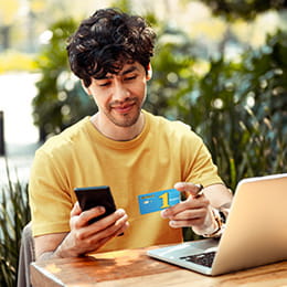 Young man looking at this credit card and entering information on his cellphone.