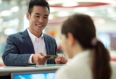 Smiling man standing at a high counter handing a Golden 1 credit card for payment.