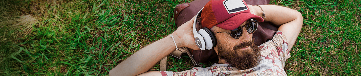 Man with headphones wearing a hat laying in the grass