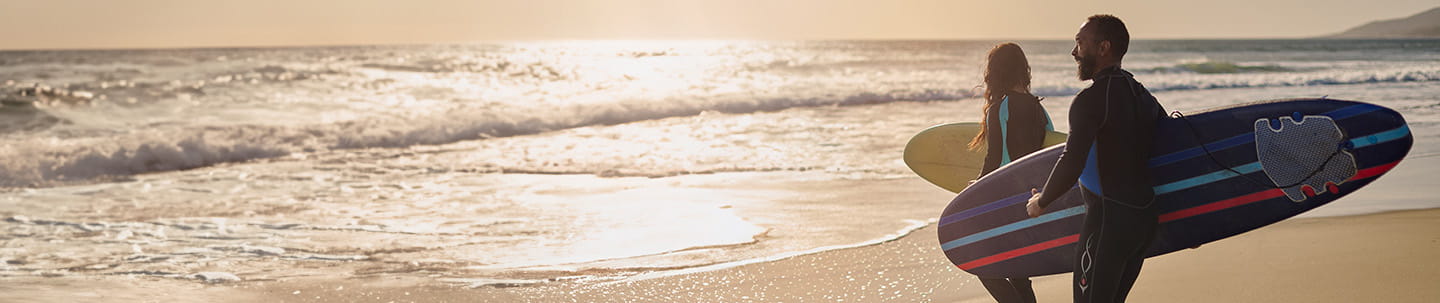 A couple walking into the beach with surfboards