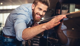 Smiling man closely admiring the finish on a car