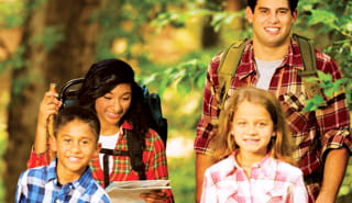 Man and woman wearing backpacks, and boy and girl all hiking in woods
