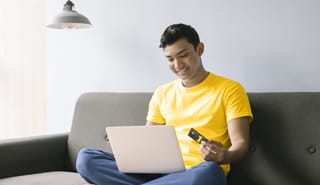 Smiling young man sitting on couch with device in lap