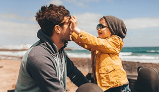 Dad at beach with son touching dad's glasses