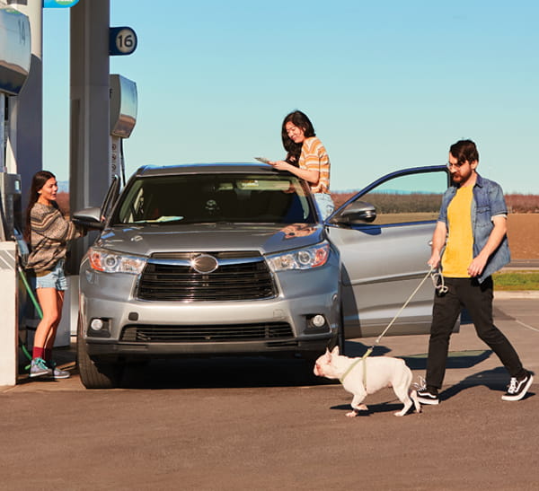 Group of young people standing around a car while at a gas pump