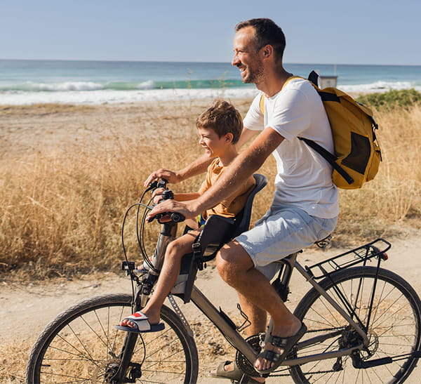 Father and son riding a bicycle along a beach shoreline.