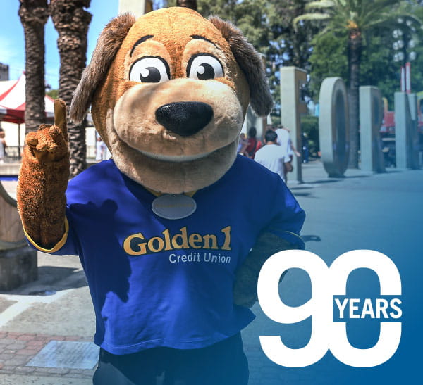 "Goldie" golden retriever mascot character holding up one finger, overlaid by logo that says "90 years"