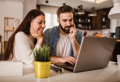 Woman and man sitting at kitchen counter looking at laptop screen