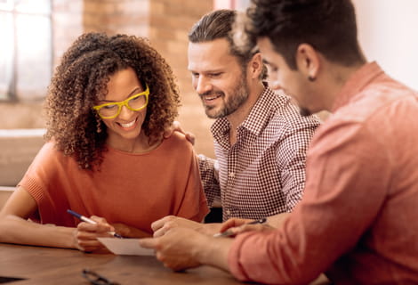 Smiling woman and two men sitting at a table reviewing a document together